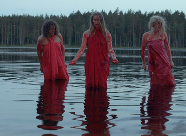 Three female figures in red dresses stand in water up to their knees