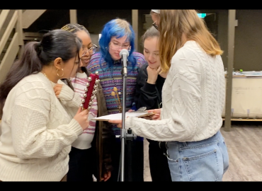five students standing around a microphone reading a clip board