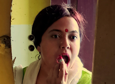 Woman wearing bindi looking in mirror and applying lipstick