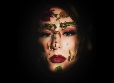 Woman&amp;#039;s face on black background with leaves and stems on forehead, nose and cheeks