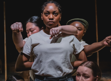 One actor stands looking outwards towards audience while four actors stand behind or  beside them with arms reaching out in scene from Conjugal play.  